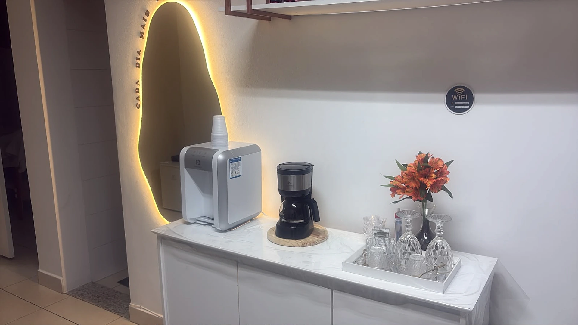 Espaço de acolhimento da clínica com espelho iluminado e área de café